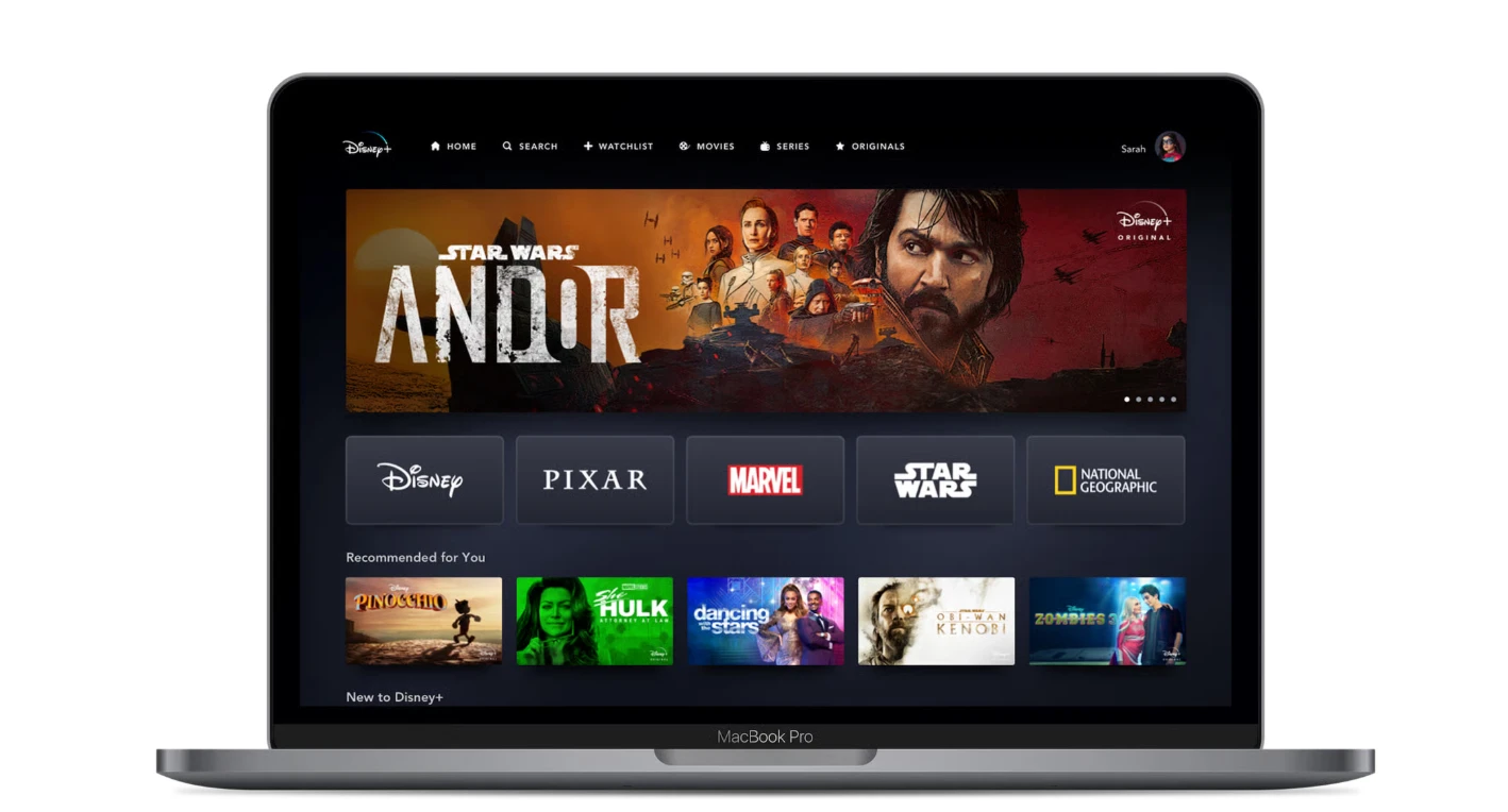 The Disney+ app home screen on a laptop, showing featured titles and brand tiles